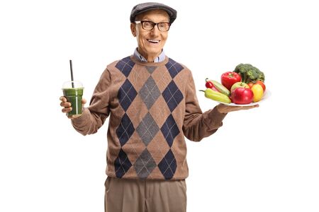 Elderly man holding a plate of fresh fruits and vegetables and a green smoothie isolated on white backgroundの写真素材