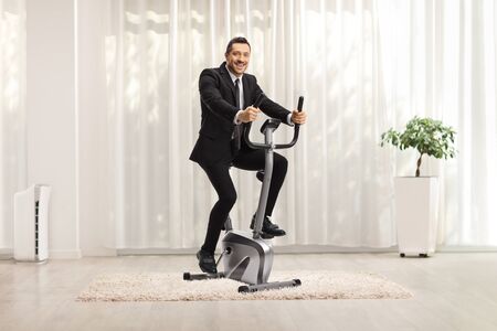 Businessman on an exercise bike at homeの写真素材