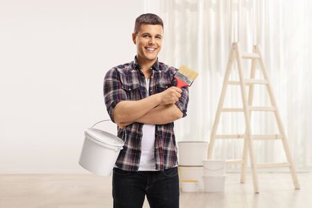 Man with a brush and a color bucket posing in a room with ladderの写真素材
