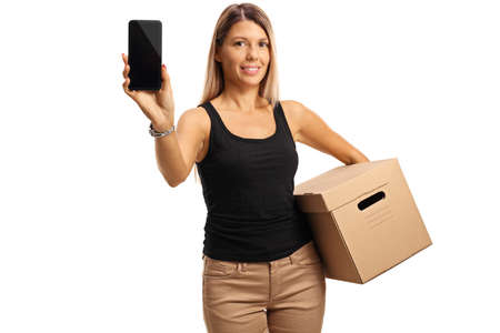 Young woman holding a cardboard box and showing a mobile phone isolated on white background