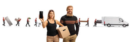 Bearded young man and a woman with a cardboard box and a mobile phone with movers and van behind...