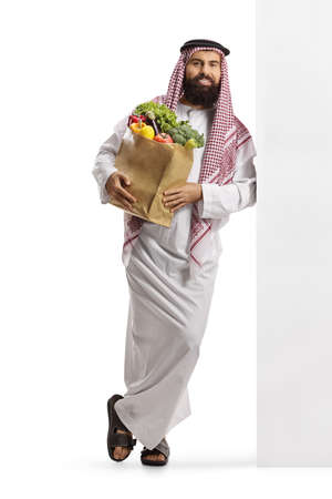 Arab man with a grocery bag standing and leaning on a wall isolated on white backgroundの写真素材