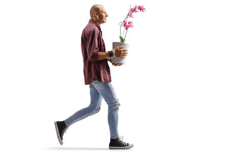 Full length profile shot of a hipster man walking and carrying an orchid flower pot isolated on white backgroundの写真素材