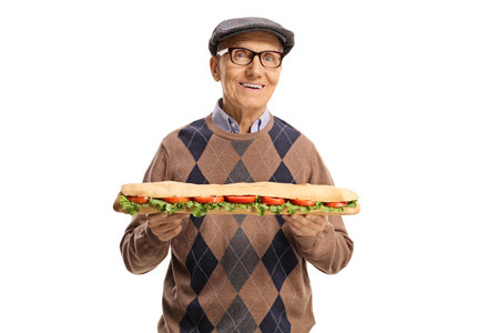 Elderly man holding a tasty long sandwich in a baguette and smiling at camera isolated on white backgroundの写真素材