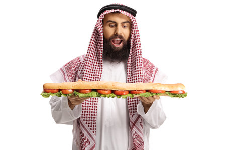 Excited arab man holding a tasty long sandwich in a baguette isolated on white backgroundの写真素材