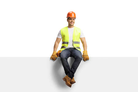 Construction worker with a helmet sitting on a blank panel isolated on white backgroundの写真素材