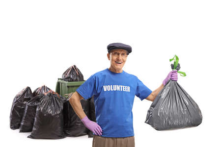 Elderly male volunteer holding a plastic waste bag in front of a dust bin isolated on white backgroundの写真素材