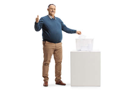 Mature citizen casting a vote in a ballot box and showing thumbs up isolated on white backgroundの写真素材