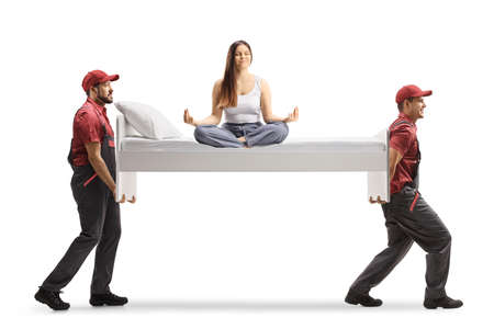 Movers carrying a bed with a young female in pajamas sitting in a yoga pose isolated on white backgroundの写真素材