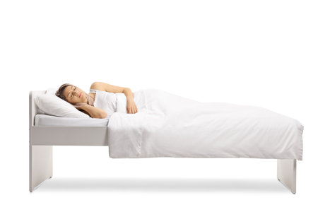 Young woman sleeping peacefully in a single bed under a white duvet cover isolated on white backgroundの写真素材