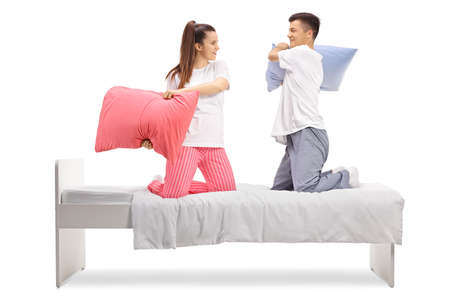 Young man and woman in pajamas fighting with pillows on a bed
