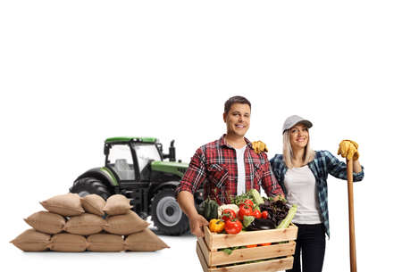 Young male and female farmers with a tractor and a crate with vegetables isolated on white backgroundの写真素材