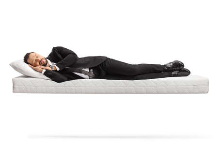 Businessman in a suit and tie sleeping on a floating mattress isolated on white backgroundの写真素材