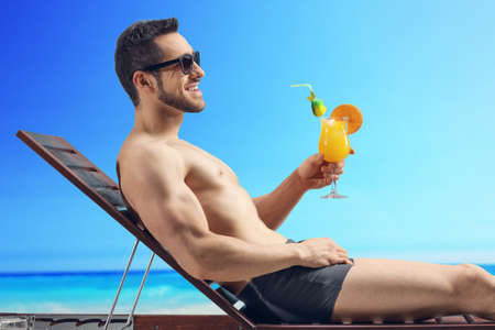 Man sunbathing and holding a cocktail by the seaの写真素材