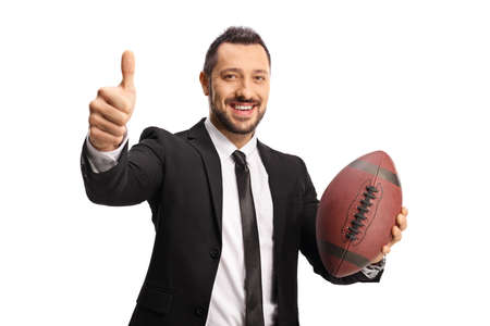 Smiling businessman holding a rugby ball and gesturing thumbs up isolated on white backgroundの写真素材
