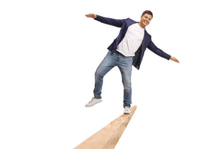 Full length shot of a young man walking on a wooden beam and keeping balance isolated on white...