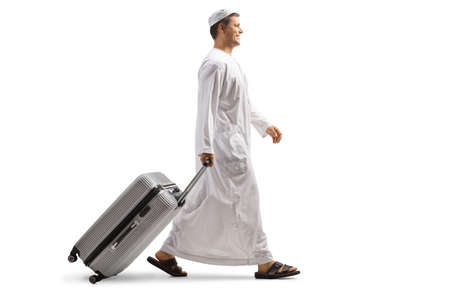 Full length profile shot of a man in ethnic clothes pulling a suitcase and walking isolated on white backgroundの写真素材