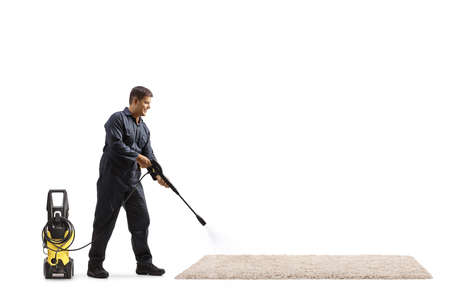 Full length shot of a male worker cleaning a carpet with a pressure washer machine isolated on white backgroundの写真素材