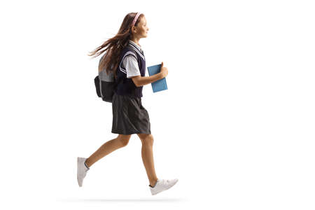 Full length profile shot of a schoolgirl with long hair carrying a book and running isolated on white backgroundの写真素材