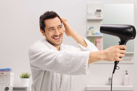 Young man in a bathrobe drying his hair inside a bathroomの写真素材
