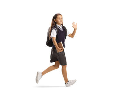 Schoolgirl carrying a book, waving and running isolated on white backgroundの写真素材