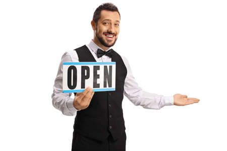 Cheerful young waiter holding a sign open and gesturing welcome isolated on white background