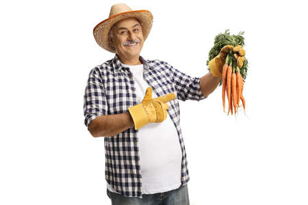 Farmer holding fresh organic carrots and pointing isolated on white backgroundの写真素材