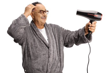 Smiling mature man wearing a bathrobe and using a hair dryer isolated on white backgroundの写真素材