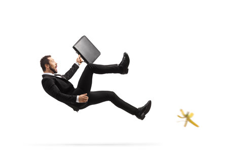 Businessman with a briefcase slipping on a banana peel isolated on white backgroundの写真素材