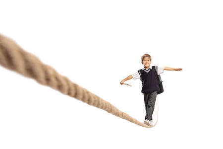 Schoolboy in a uniform holding a book and walking on a rope isolated on white background