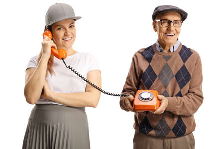 Elderly man holding a vintage rotary phone and a young female talking isolated on white backgroundの写真素材