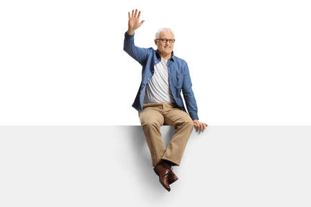 Mature man with white hair and casual clothing sitting on a blank panel and waving isolated on white backgroundの写真素材