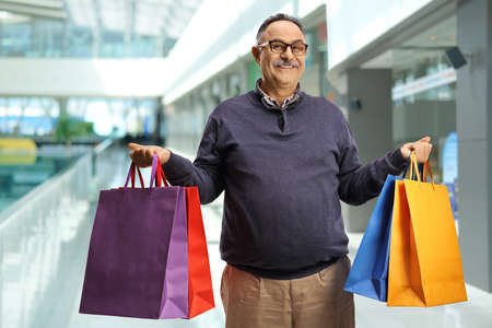Mature man holding shopping bags and smiling inside a shopping mallの写真素材