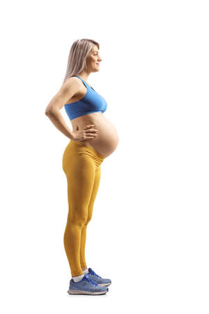Full length profile shot of a pregnant woman in a blue crop top and yellow leggings isolated on white backgroundの写真素材