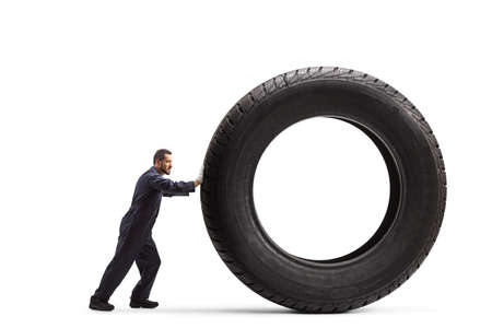 Full length profile shot of a mechanic pushing a big vehicle tire isolated on white background