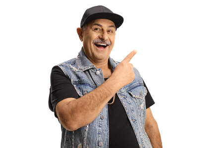 Cheerful mature man in a denim vest and cap smiling and pointing isolated on white background