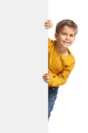 Cute boy peeking from behind a blank white panel isolated on white backgroundの写真素材