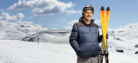 Mature man smiling and holding a pair of skis on a mountainの写真素材