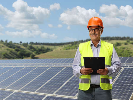 Smiling mature male engineer standing in front of solar panels in a field
