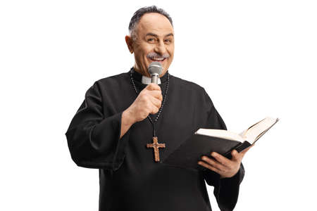 Mature priest reading a prayer from the bible and holding a microphone isolated on blue background