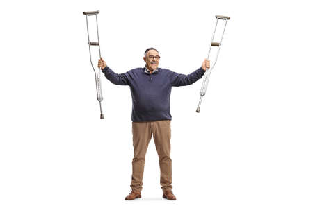Happy mature man holding crutches up after recovery isolated on white backgroundの写真素材