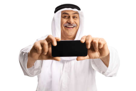 Smiling mature arab man taking a photo with a smartphone isolated on white backgroundの写真素材