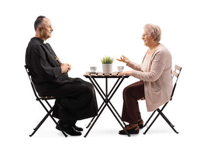 Priest and an elderly woman sitting at a table with coffee and talking isolated on white backgroundの写真素材