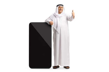 Mature arab man leaning on a big smartphone and showing thumbs up isolated on white background
