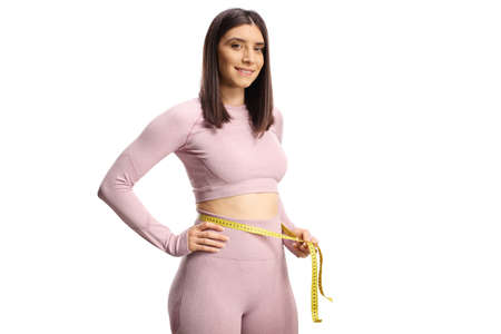 Fit woman in sportswear measuring her waist and smiling at camera isolated on white background