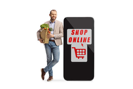 Full length portrait of a young man holding a grocery bag and leaning on a smartphone with text shop...