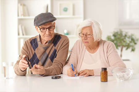 Elderly man and woman sitting at home with medications on a table and checking blood sugar levelの写真素材