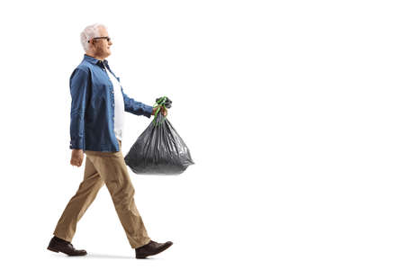 Full length profile shot of a mature man walking and carrying a plastic waste bag isolated on white backgroundの写真素材