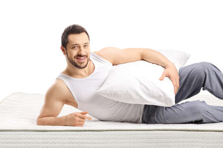 Man lying on a mattress and holding a pillow isolated on white backgroundの写真素材