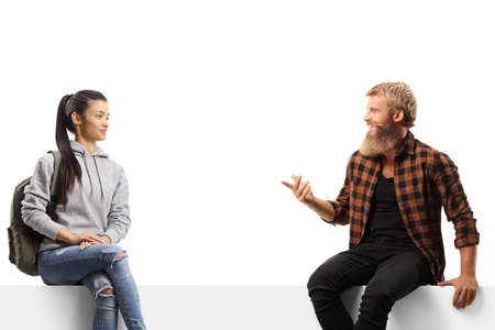 Bearded man sitting on a white panel and talking to a female student isolated on white background